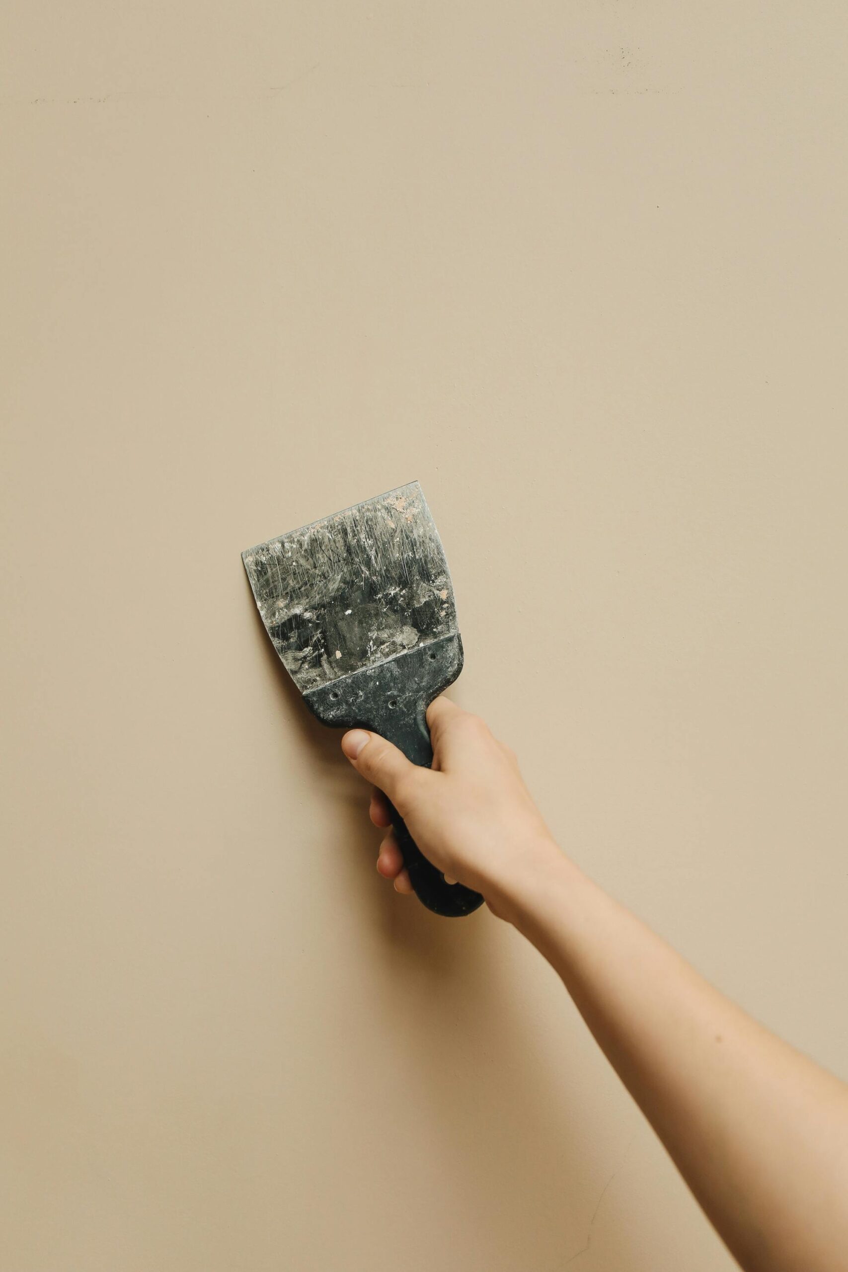 A hand holding a putty knife against a wall, ideal for renovation themes.